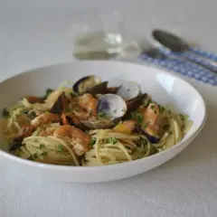 Un plato de spaghetti frutti di mare con gambas, mejillones y almejas, adornado con perejil fresco.