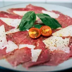 Carpaccio de ternera con queso parmesano, hojas de albahaca y tomates cherry cortados por la mitad.