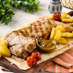 Jugosa carne al ajillo, servida con patatas rústicas y salsa, sobre papel de periódico. ¡Un festín para los sentidos!