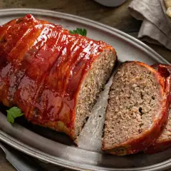 Un jugoso pastel de carne cubierto de glaseado rojo brillante, envuelto en tocino y servido en una bandeja de plata.