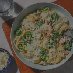 Un plato de pasta carbonara con huevo, brócoli y queso rallado, listo para disfrutar.