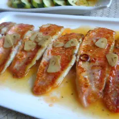 Deliciosos salmonetes a la plancha con láminas de ajo y un toque de guindilla, servidos en una salsa dorada.