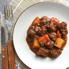 Un plato de goulash de ternera con trozos de patata y zanahoria, adornado con cebollino. Cubiertos de una rica salsa.