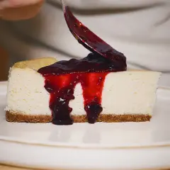 Un trozo de new york cheesecake cremoso con salsa de frutos rojos cayendo.