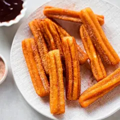 Churros sin gluten espolvoreados con azúcar y canela, servidos con chocolate caliente.
