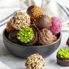 Un tazón lleno de deliciosas trufas de chocolate, algunas cubiertas de frutos secos, otras con chispas de colores y pistachos.