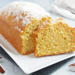 Bizcocho de coco esponjoso, cubierto con coco rallado, servido en una bandeja blanca.