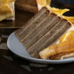 Rebanada de tarta de plátano con capas de bizcocho y crema, decorada con trozos de plátano caramelizado.