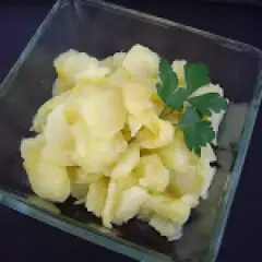 Un cuenco de cristal contiene patatas al montón, un plato sencillo y reconfortante, adornado con una ramita de perejil fresco.