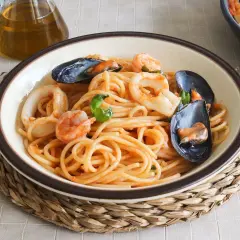 Un plato de espaguetis a la marinera con gambas, calamares y mejillones, servido en un cuenco sobre una esterilla de mimbre.