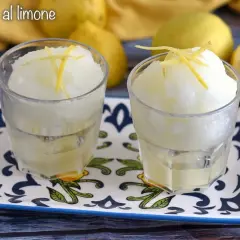 Dos vasos de refrescante helado de limón, adornados con ralladura de limón, sobre una bandeja decorada.