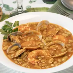 Plato de verdinas con almejas y gambas, decorado con perejil. Acompañado de pan en cesta.