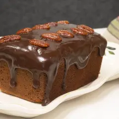 Bizcocho de platano y chocolate cubierto de glaseado y nueces pecanas, listo para disfrutar.