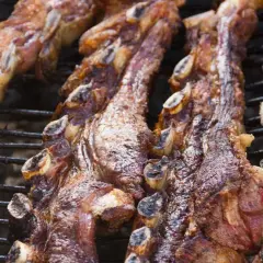 Costillas de churrasco a la plancha, doradas y jugosas, cocinándose lentamente sobre la parrilla.