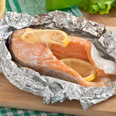 Salmón jugoso en papel de aluminio con rodajas de limón y romero.