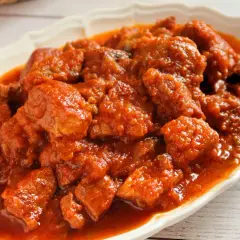 Magro con tomate en un plato blanco, con trozos de carne en salsa roja.
