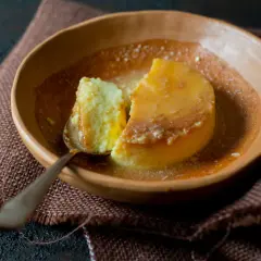 Un trozo de flan de yogur cremoso, bañado en caramelo líquido, servido en un cuenco de barro.