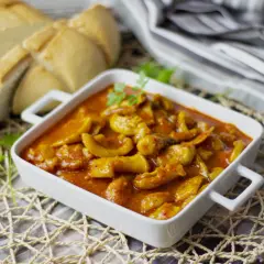 Deliciosa jibia en salsa, servida en un cuenco blanco, acompañada de pan rústico y hojas de laurel.