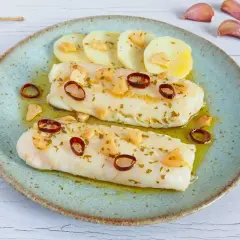 Dos lomos de merluza a la bilbaina, con patatas, ajo laminado y guindilla, servidos en plato azul.