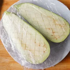 Dos mitades de berenjena cortadas en cubos y cubiertas con plástico, listas para cocinar berenjenas al microondas.