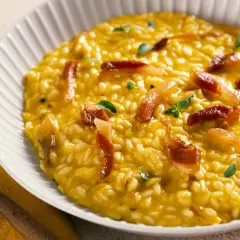 Cremoso risotto de queso, con trozos de panceta crujiente y hojas verdes.