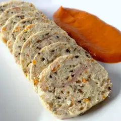 Fiambre de pollo casero en rodajas, con trocitos de verdura y jamón, acompañado de una salsa naranja.