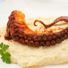 Un tentáculo de pulpo a la plancha, crujiente y especiado, reposa sobre un puré cremoso.