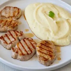 Cinco medallones de solomillo a la parrilla con puré de patatas cremoso, decorado con una ramita de perejil.