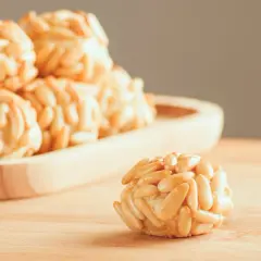 Rosquillas de naranja cubiertas de piñones, con un dulce aroma cítrico y un crujiente exterior.