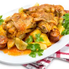 Manitas de cerdo receta tradicional de la abuela, con patatas y chorizo, servido en plato blanco con perejil fresco.