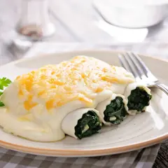 Canelones de espinacas cubiertos con bechamel y queso gratinado, servidos en un plato con perejil fresco.