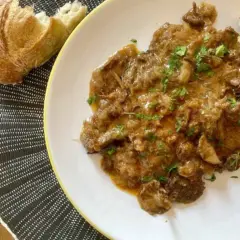 Plato de fricando de ternera con salsa cremosa y trozos de pan crujiente.