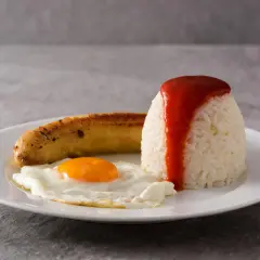 Un plato de arroz a la cubana con huevo frito y salchicha, cubierto con salsa de tomate.