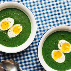 Dos cuencos de espinacas a la crema con huevos duros cortados por la mitad, servidos sobre un mantel de cuadros azules y blancos.