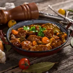 Caldereta de cordero humeante, con trozos de carne tierna, zanahoria y brócoli, servida en una cazuela rústica.