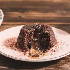 Coulant de chocolate con centro líquido y cremoso, espolvoreado con cacao en polvo sobre un plato rosa.