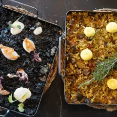 Dos arroces a la llauna: uno negro con calamares y alioli, y otro dorado con verduras y romero.