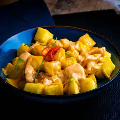 Patatas bravas receta: trozos dorados de patata cubiertos con una cremosa salsa rosada y decorados con pimiento rojo y cebollino.