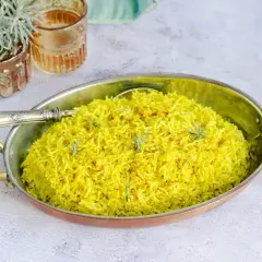 Un aromático arroz al curry, teñido de un vibrante amarillo por la cúrcuma y decorado con hebras de azafrán y romero fresco.