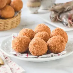 Croquetas de gambas doradas y crujientes en un plato, con gambas crudas al fondo.