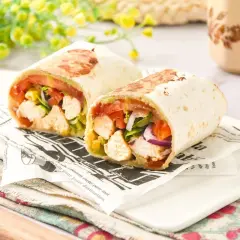 Dos burritos de pollo cortados por la mitad, rellenos de pollo, tomate, lechuga y cebolla morada, servidos sobre papel de periódico.