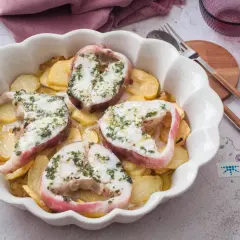 Rodajas de pescado rosado al horno con patatas, cubiertas de hierbas frescas.