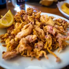 Plato de puntillas de calamar fritas, crujientes y doradas, servido con una rodaja de limón.