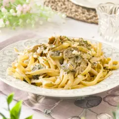 Pasta con setas cremosa, servida en un plato decorado, con un tenedor de bronce al lado.