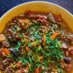 Un reconfortante potaje de lentejas con trozos de chorizo, zanahoria y perejil fresco, servido en un cuenco amarillo.