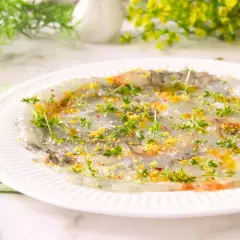 Delicado carpaccio de gambas con hierbas frescas y ralladura de limón, listo para disfrutar.