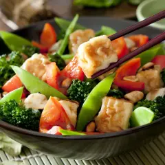 Un delicioso salteado de verduras con brócoli, pimientos rojos y guisantes dulces, servido en un cuenco oscuro.