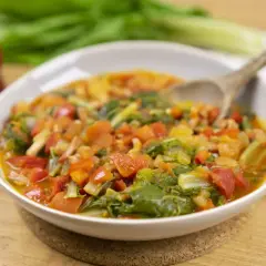 Un plato humeante de guiso de verduras, ideal para recetas con acelgas. Contiene trozos de tomate, pimiento rojo y hojas verdes.