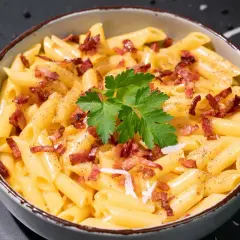 Un tazón de macarrones a la carbonara, cubiertos con trozos de tocino crujiente, perejil fresco y pimienta negra.