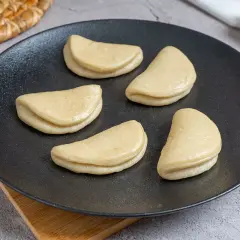 Cinco panes bao crudos en un plato negro, listos para la receta.